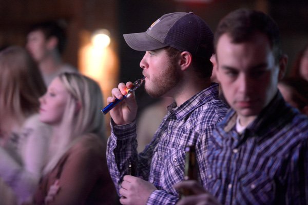 Jesse McCoy, of Bentonville, smoke an electronic cigarette Thursday, Dec. 12, 2013 during a concert at George's Majestic Lounge in Fayetteville. Electronic cigarettes have risen in popularity recently, but where they fall on health concerns and public smoking ordinances is confusing to some.