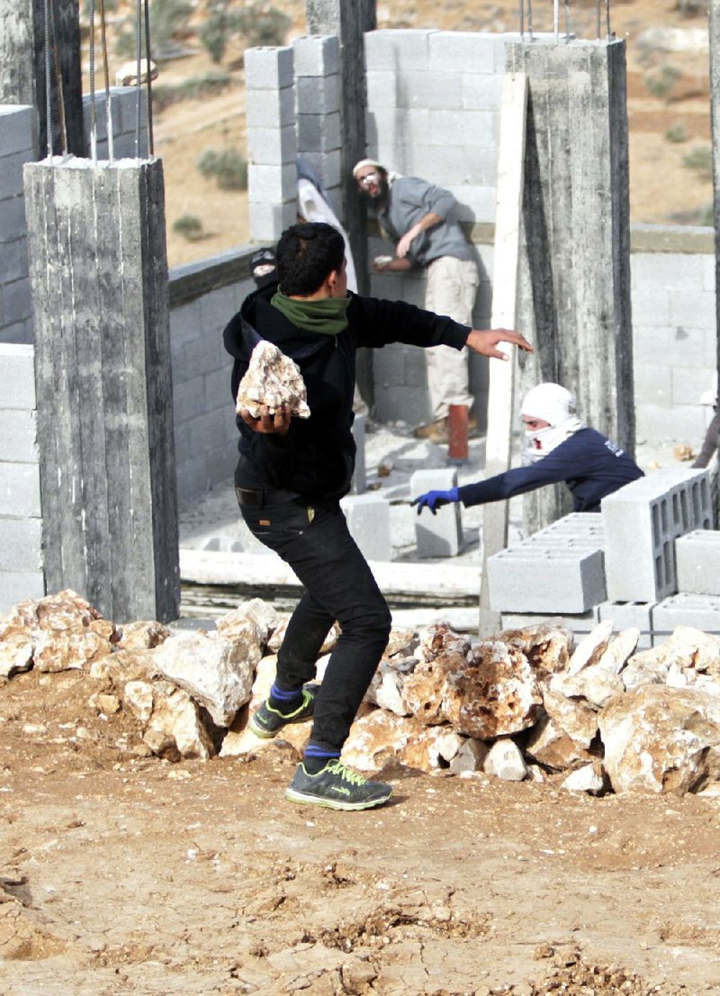 A Palestinian throws stones at Israeli settlers Tuesday in a building under construction near the West Bank village of Qusra before they were detained. The settlers reportedly had earlier attacked Palestinian farmers. 