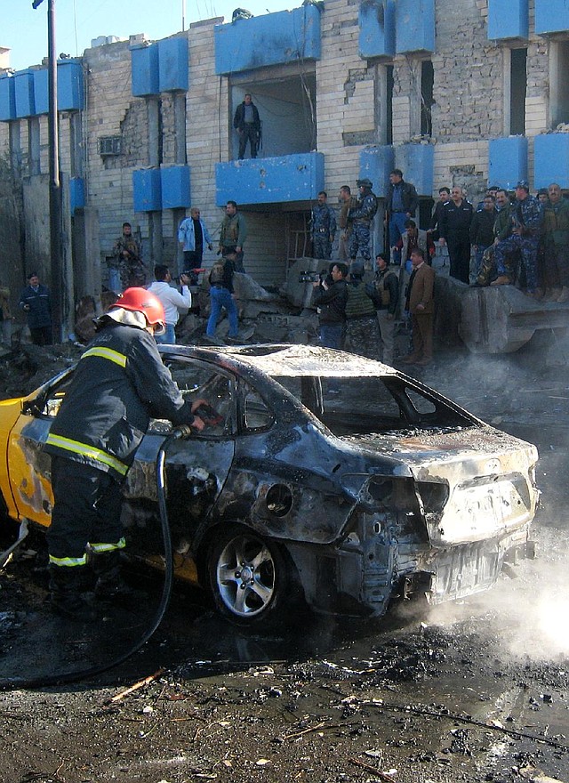 An Iraqi firefighter hoses down a car that caught fire Tuesday after a truck loaded with explosives rammed into a police station in Kirkuk. 