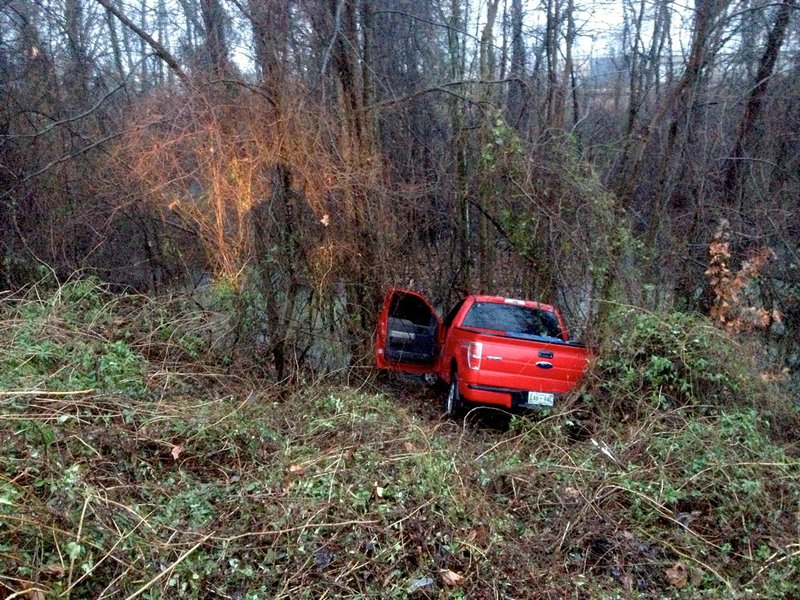 A pickup sits crashed in a wooded area after sliding Friday, Jan. 10, 2014, off a wet Interstate 440 in Little Rock.