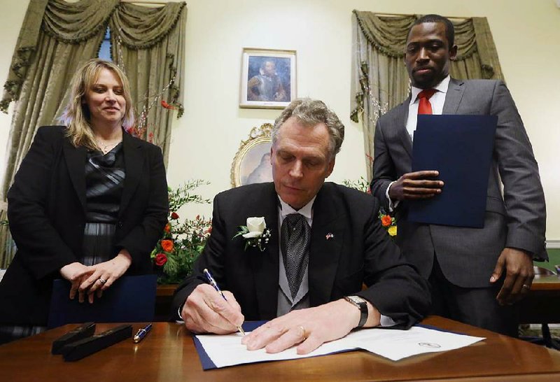 Virginia Gov. Terry McAuliffe, center, signs his first executive orders, flanked by former Secretary of the Commonwealth Janet Kelly, left, and incoming Secretary of the Commonwealth Levar Stoney, right, inside the State Capitol in Richmond, Va., Saturday, Jan. 11, 2014.  (AP Photo/Bob Brown, Pool)