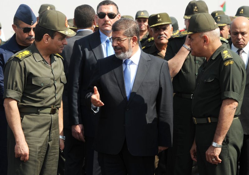 FILE - In this Wednesday, Oct. 10, 2012 file image, then-Egyptian President Mohammed Morsi, center, speaks with Minister of Defense, Lt. Gen. Abdel-Fattah el-Sissi, left, at a military base in Ismailia, Egypt. The country's ousted Islamist President and 24 other politicians, media personalities, activists and lawyers will be tried on charges of insulting the judiciary.(AP Photo/Egyptian Presidency, File)