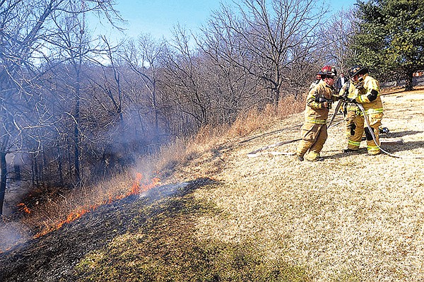 STAFF PHOTO FLIP PUTTHOFF 
Rogers firefighters bring a hose to a grass and brush fire Tuesday in the Summit Heights area of Rogers, east of downtown. The fire burned grass and woods in a hollow between Summit Heights and Lake Atalanta.