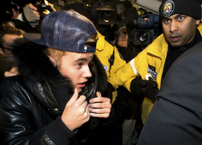 Canadian musician Justin Bieber is swarmed by media and police officers as he turns himself in to city police for an expected assault charge in Toronto on Wednesday, Jan. 29, 2014. A police official said the charge has to do with an alleged assault on a limo driver in December. 
