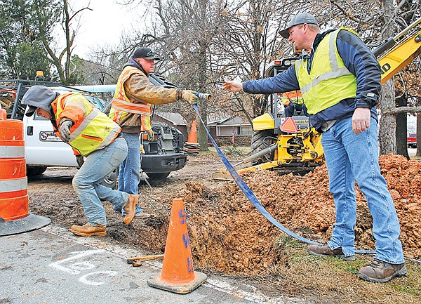 STAFF PHOTO DAVID GOTTSCHALK 
Dan Jones, right, distribution manager with Springdale Water Utilities, reaches over for a drainage hose Friday from Randy Rogers, distribution operator, as Jeremy Mounce, distribution operator, climbs out of a ditch on 56th street in Springdale near County Line Road. The crew repaired a 1-inch service line coming off of a main water line with a leak.