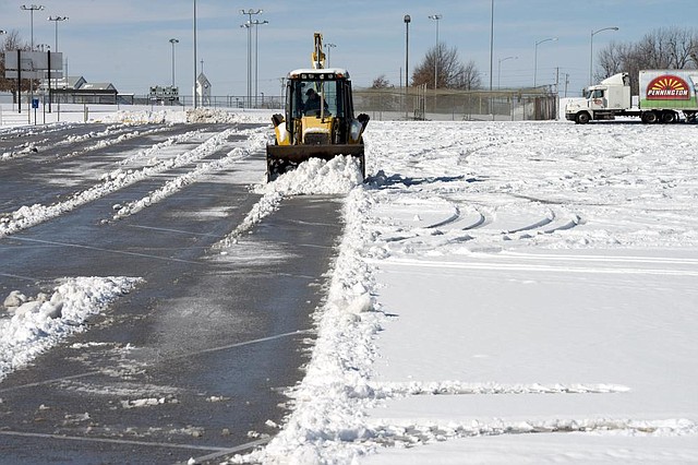 A backhoe scraps snow off a parking lot Monday, Feb. 3, 2014 at the Tyson Sports Complex in Springdale. Crews had to work to clear away snow after a winter snow dumped more than three inches on Springdale. More winter weather is expected today. 