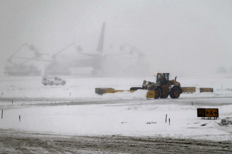 A snow plow clears the runways as a plane is de-iced, Monday, Feb. 3, 2014 at Newark Liberty International Airport in Newark, NJ.  Air traffic is disrupted in Ohio, the Mid-Atlantic and the Northeast as another winter storm bears down on the eastern U.S., only a day after temperatures soared into the 50s.   (AP Photo/Matt York)