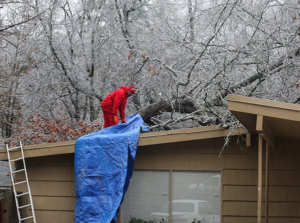 Arkansas Democrat-Gazette/STATON BREIDENTHAL
Roy Cranford covers a hole in his roof Tuesday after an ice-laden tree fell on the house on Edgemont Drive in Little Rock. No one was home when the tree gave way, Cranford said. While road crews dealt with ice, snow, freezing rain and sleet across much of the state, ice accumulation was heavy in central Arkansas.