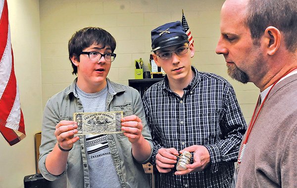 STAFF PHOTO FLIP PUTTHOFF 
Noah Smith, left, shows Wednesday some replica Civil War era currency while classmate Hunter Satterfield, center, sports a Union soldier’s hat. Danny Burdess, right, history teacher, listens to the presentation about the students’ Civil War project.