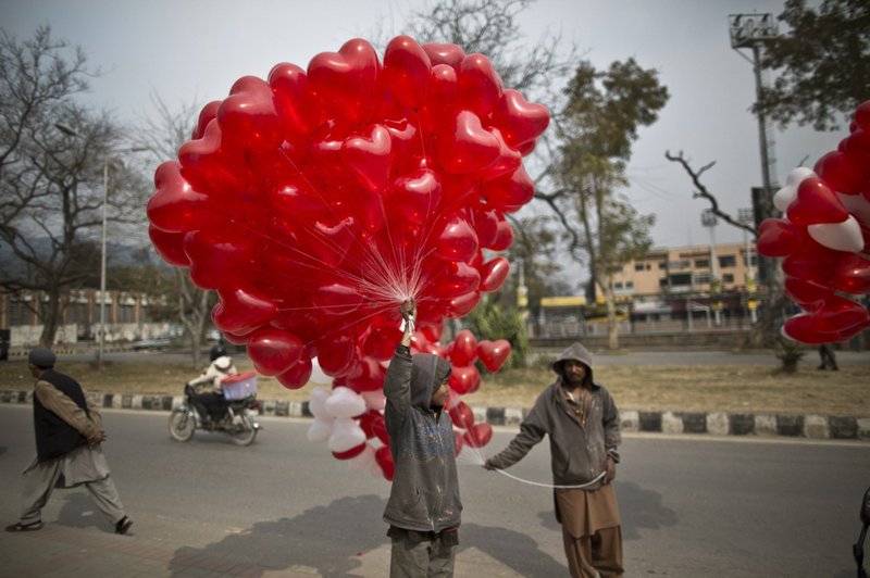 A Pakistani boy stands on a roadside along with other vendors, holding red heart-shaped balloons hoping to sell them on Valentine's Day in Islamabad, Pakistan, on Friday, Feb. 14, 2014. 