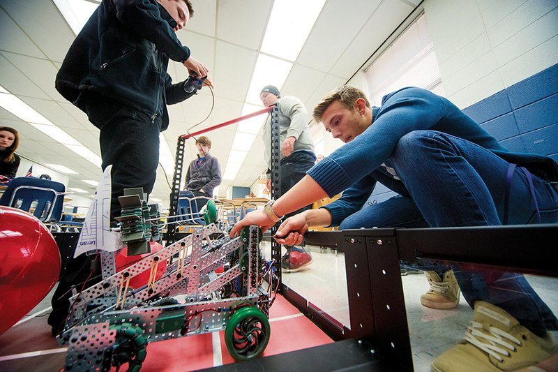 From the left, Rex Hearn holds a remote control as Dylan Wilcox and Buddy Williams watch Nick Gatlin prepare a robot for practice. They are members of the Hornet Engineering and Technology team at Bryant High School.