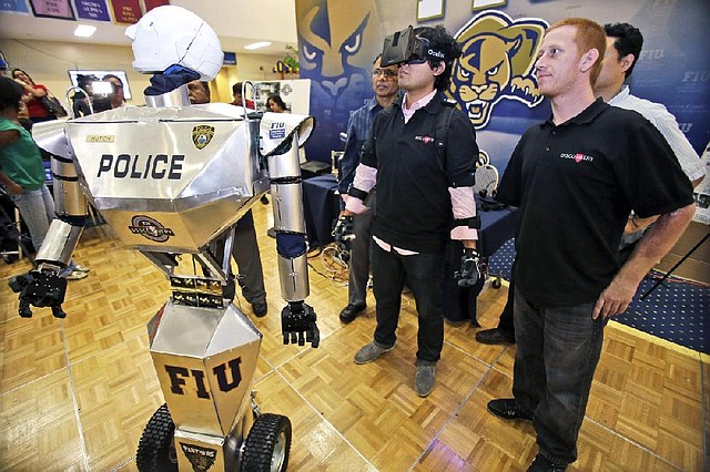 Student Jamie Danow, right, 28, looks on as Irvin Cardenas, second from right, 22,  controls a TeleBot, which combines telepresence and robotics, with sensors placed around his body, during a demonstration at Florida International University, Wednesday, Feb. 12, 2014 in Miami. A group of students at FIU's Discovery Lab is testing their version of a RoboCop that will allow disabled police and military personnel to serve as patrol officers. Danow, who lost his right arm in a motorcycle accident in 2006 and can no longer bend his left elbow, is in charge of developing the user interface for people missing their upper extremities. "This is perfect for me," Danow explained he felt before joining the team. "I never could have imagined I would have this opportunity. Things happen sometimes maybe for a reason and you don't realize that." (AP Photo/Wilfredo Lee)