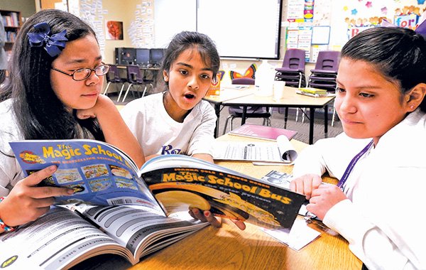 STAFF PHOTO BEN GOFF 
Sixth-grade tutor Brianna Hernandez, 12, from left, reads “The Magic School Bus: Lost in the Solar System” on Thursday with fifth-graders Madhura Srinivas, and Michelle Gonzalez, both 10, as part of the Learning Together program at Ruth Barker Middle School in Bentonville.