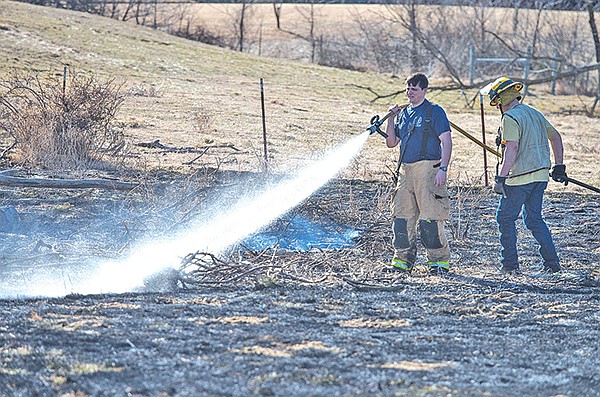 STAFF PHOTO ANTHONY REYES 
Capt. Jo Kidd, left, and firefighter Derek Crutchfield, both with the Tontitown Area Fire Department, fight a grass fire Friday off Osage Creek Road in Tontitown.