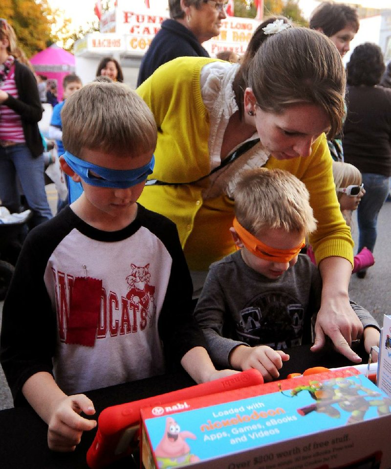 Wearing Teenage Mutant Ninja Turtles masks given out by a vendor, brothers Logan Colburn, 7, and Benjamin Colburn, 4, and their mother, Sarah Colburn, all of Centerton check out children’s computer tablets at a First Friday event in Bentonville on Nov. 1. 