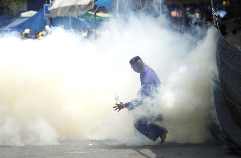 An anti-government protester is caught in tear gas during clashes with riot police in Bangkok on Tuesday. Clashes between police and anti-government demonstrators in Bangkok left four people dead and dozens injured Tuesday as riot police attempted to clear out protest camps around the Thai capital. 