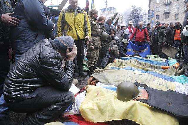 Activists pay respects to protesters killed in clashes with police, during clashes with riot police in Kiev's Independence Square, the epicenter of the country's current unrest, Thursday, Feb. 20, 2014. The flag held by one activist at rear reads 'For Ukraine.' Fierce clashes between police and protesters in Ukraine's capital have shattered the brief truce Thursday and an Associated Press reporter has seen dozens bodies laid out on the edge of the protest encampment.  (AP Photo/Efrem Lukatsky)