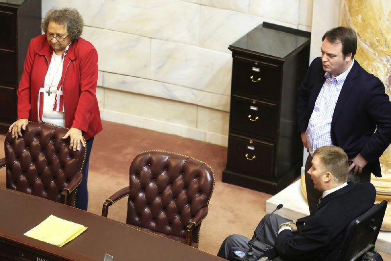 Rep. Sheilla Lampkin D-Monticello gathers with Rep. John Burris (standing) R-Harrison and Rep. Josh Miller R-Heber Springs behind the empty chair of Rep. John Payton, R-Wilburn, who was supposed to be present to cast a “paired” House vote on the private-option funding measure but could not be found. 