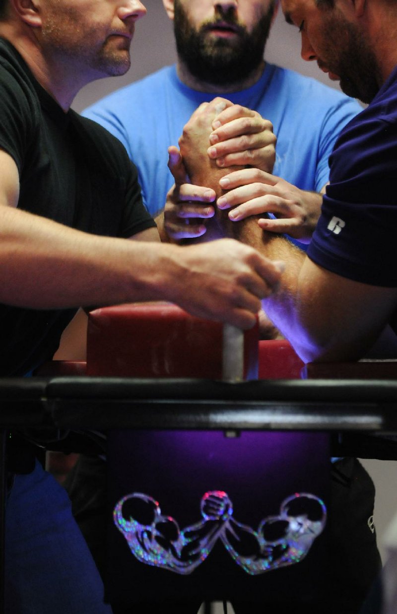 STAFF PHOTO SAMANTHA BAKER w @NWASAMANTHA
David Finkbeiner, center, positions Scott Fleming, left, of Oak Grove, Mo. and Bruce Jones of Beebe for competition Saturday, Feb. 8, 2014, at Inferno Fitness & Mixed Martial Arts in Springdale during the Border Wars Challenge Winter Throwdown arm wrestling tournament. The competition was double-elimination for each of the four men's weight divisions and open women's divisions.