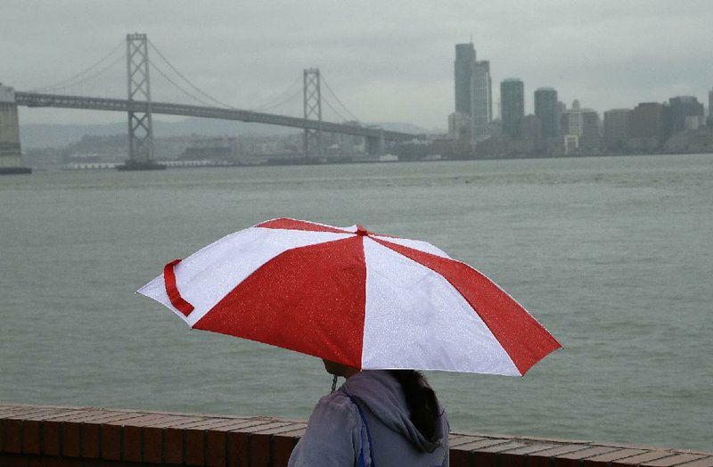 A woman walks along Treasure Island with the San Francisco Bay Bridge in the background during a rainstorm Wednesday in San Francisco where more rainfall was expected through the week. 