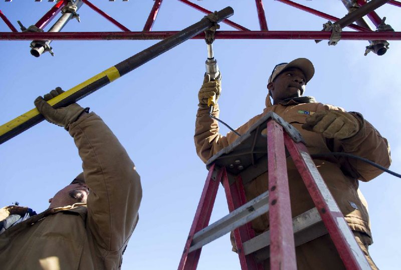 Little Rock Parks and Recreation Department worker Ed Barnes (left) holds a support beam Wednesday for fellow worker Titus Jordan before it is secured to a structure used for various equipment at the finish line of the Little Rock Marathon in Riverfront Park. 