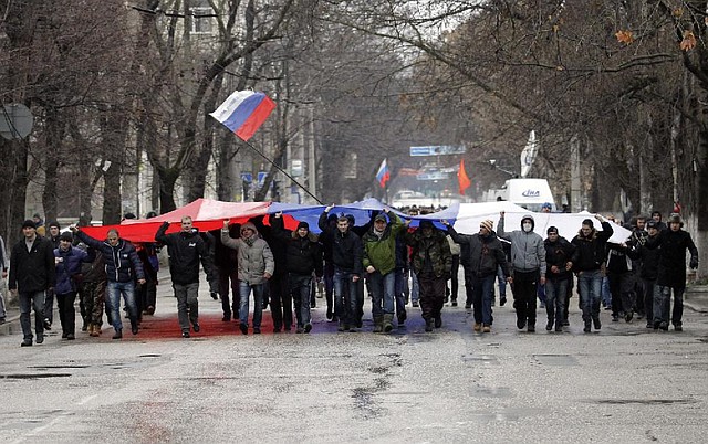 Pro-Russian demonstrators march with a huge Russian flag during a protest in front of a local government building in Simferopol, Crimea, Ukraine, Thursday, Feb. 27, 2014. Ukraine's acting interior minister says Interior Ministry troops and police have been put on high alert after dozens of men seized local government and legislature buildings in the Crimea region. The intruders raised a Russian flag over the parliament building in the regional capital, Simferopol, but didn't immediately voice any demands. (AP Photo/Darko Vojinovic)