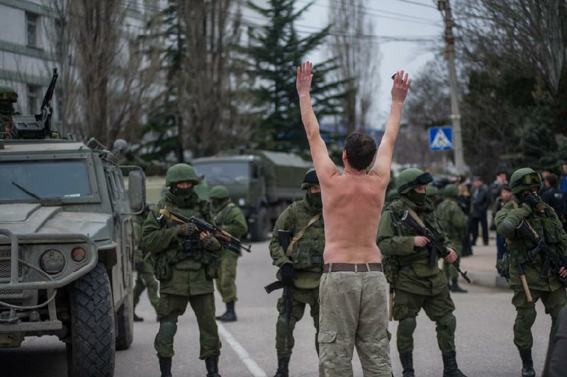 A Ukrainian man stands in protest in front of gunmen in unmarked uniforms as they stand guard in Balaklava, on the outskirts of Sevastopol, Ukraine, Saturday, March 1, 2014. An emblem on one of the vehicles and their number plates identify them as belonging to the Russian military. Ukrainian officials have accused Russia of sending new troops into Crimea, a strategic Russia-speaking region that hosts a major Russian navy base. The Kremlin hasnt responded to the accusations, but Russian lawmakers urged Putin to act to protect Russians in Crimea. (AP Photo/Andrew Lubimov)