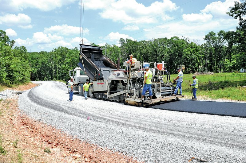 FILE PHOTO SAMANTHA BAKER Benton County&#8217;s Road Department crew lays asphalt June 19 on North Tillys Hill Road near Decatur. Justices of the peace recently agreed to cut $450,000 from the department&#8217;s 2014 budget for asphalt, dropping it from $2.65 million to $2.2 million. The money saved will be used to pay for part of rural ambulance service