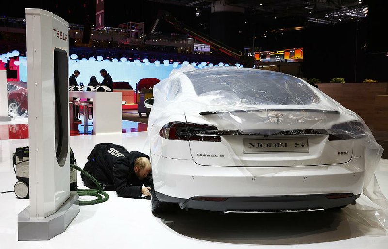 A worker checks beneath a Tesla Model S automobile, produced by Tesla Motors Inc., on the company's stand ahead of the opening day of the 84th Geneva International Motor Show in Geneva, Switzerland, on Monday, March 3, 2014. The International Geneva Motor Show will run from Mar. 4, and showcase the latest models from the world's top automakers. Photographer: Gianluca Colla/Bloomberg