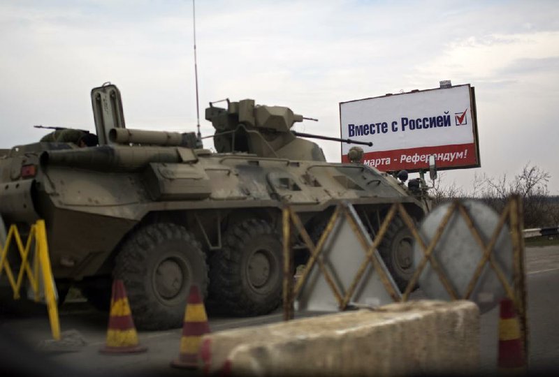 An unmarked armored personnel carrier sits Friday near a billboard proclaiming, “March 16 — Referendum! Sevastopol. Together with Russia!” at a checkpoint outside Chongar in Ukraine’s Crimea region. 