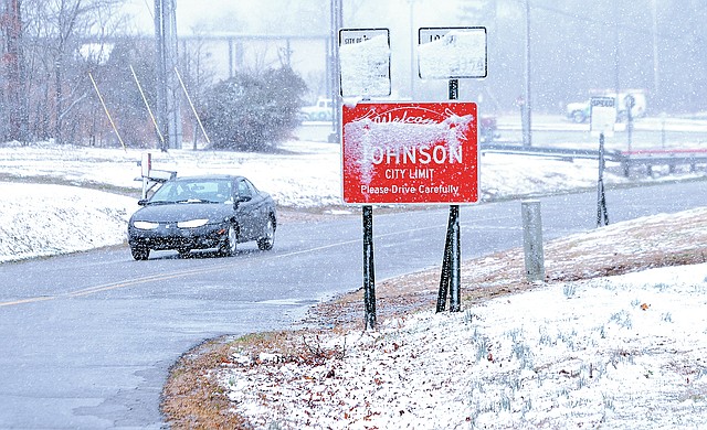 STAFF PHOTO SAMANTHA BAKER • @NWASAMANTHA A motorist drives north on South 48th Street on Sunday in Johnson while accumulating snow blocks signs along the road.