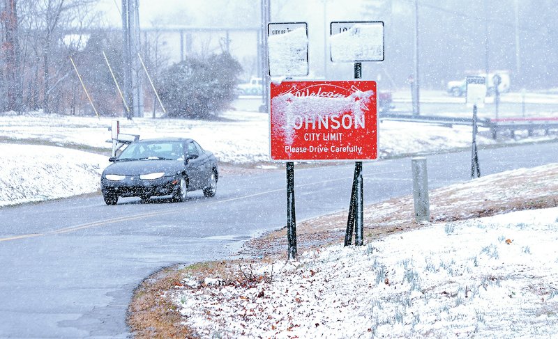 STAFF PHOTO SAMANTHA BAKER • @NWASAMANTHA A motorist drives north on South 48th Street on Sunday in Johnson while accumulating snow blocks signs along the road.