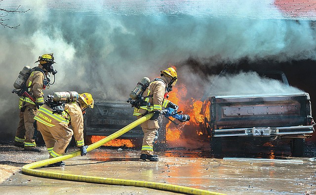 STAFF PHOTO ANTHONY REYES Springdale firefighters douse flames under a car Tuesday in the carport at 1311 Davis Ave. in Springdale. Neighbors said the fire started in the carport and high wind quickly caused the fire to spread. A neighbor noticed the fire and alerted the residents while another called the Fire Department. No one was injured in the fire.