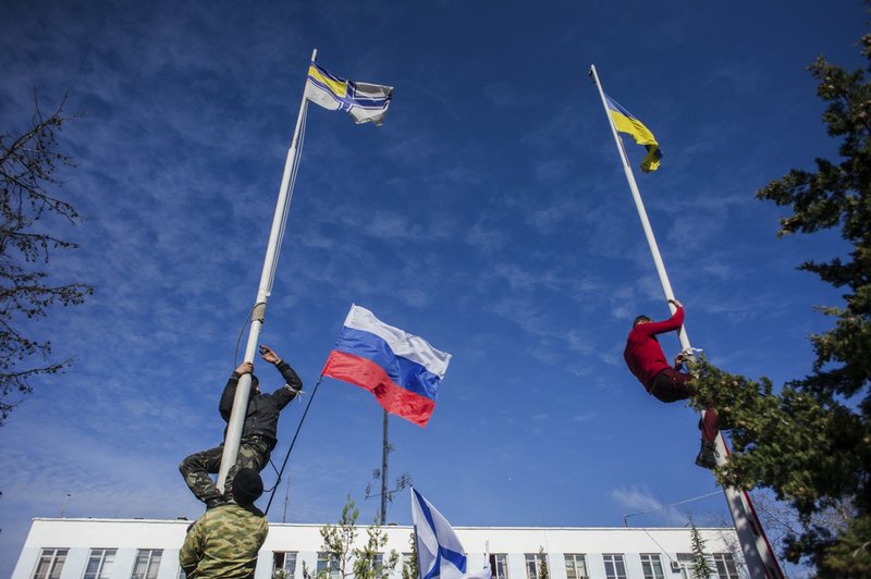 Members of the Crimean pro-Russian self-defense forces climb up to take down a Ukrainian flag, right, and a Ukrainian navy flag, left, at the Ukrainian navy headquarters in Sevastopol, Crimea, on Wednesday, March 19, 2014. Crimea's self-defense forces on Wednesday stormed the Ukrainian navy headquarters in the Black Sea port of Sevastopol, taking possession without resistance a day after Russia signed a treaty with local authorities to annex the region. In center is a Russian flag. 