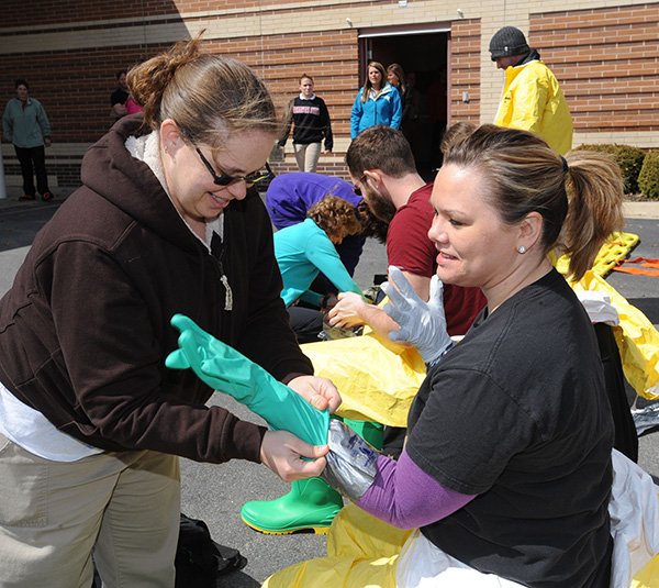 NWA Media/ANDY SHUPE 
Christina Metz (left), an emergency-room nurse at Washington Regional Medical Center, helps emergency department Assistant Director Danita Mullins put on chemical gloves during a decontamination course and demonstration Wednesday at the Fayetteville hospital. Arkansas State University’s Center for Disaster Preparedness presented the demonstration.