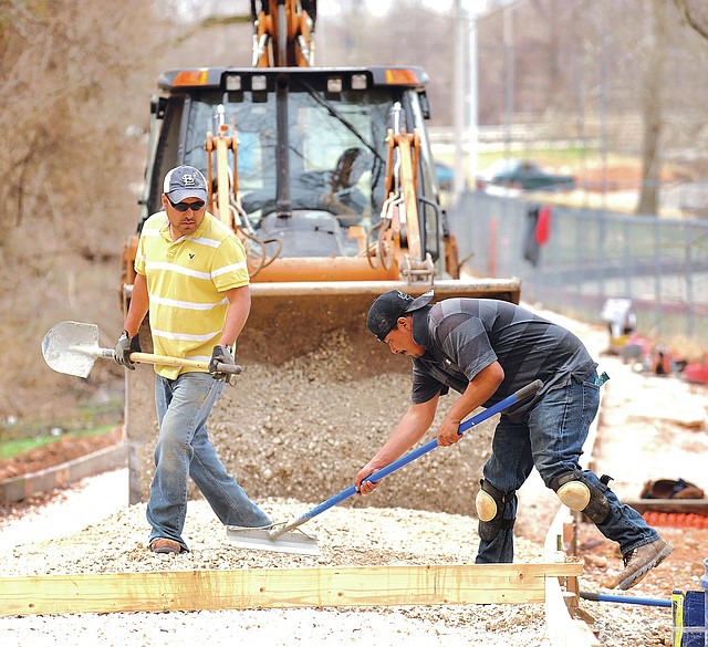 STAFF PHOTO ANDY SHUPE Jose Hernandez, left, and Javier Cisneros, both with Boulder Construction in Fayetteville, spread a gravel base Friday while preparing to pour concrete for a trail extension east of College Avenue near Lake Fayetteville.