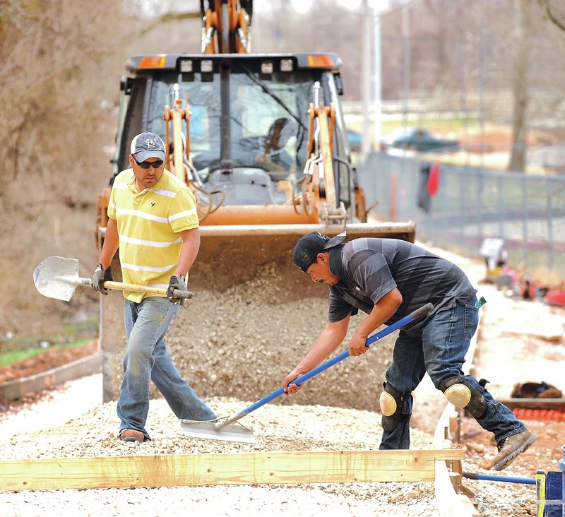 STAFF PHOTO ANDY SHUPE Jose Hernandez, left, and Javier Cisneros, both with Boulder Construction in Fayetteville, spread a gravel base Friday while preparing to pour concrete for a trail extension east of College Avenue near Lake Fayetteville.