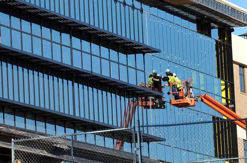 FILE PHOTO &#8212; Construction crews place glass windows on the south side of the new building under construction on the Fayetteville High School campus in January. The $93 million high school expansion was one of many public works projects that eased the building slowdown form the recession.