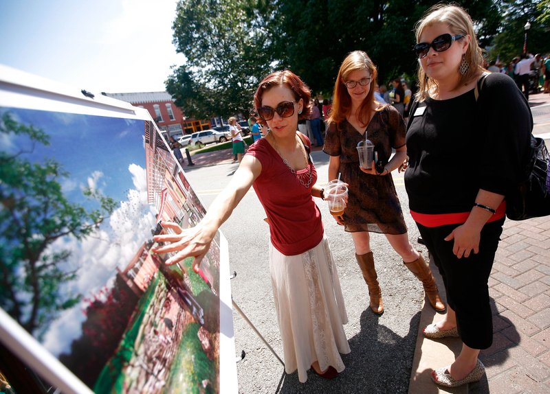 FILE PHOTO &#8212; Jessie Wagner, left, Sara Segerlin and Anne Jackson, all with Crystal Bridges Museum of American Art, look over an artist rendering following a news conference on the Bentonville square last June for the Amazeum, a children&#8217;s museum. Officials are expecting to break ground in the next couple of months on the $28 million, 44,500-square-foot facility.