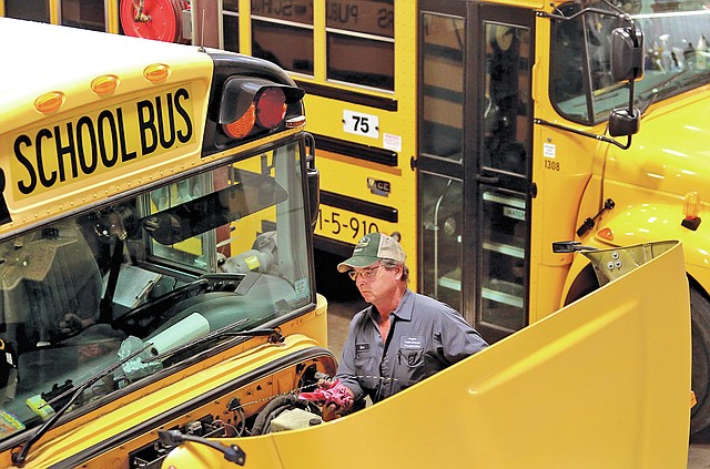 STAFF PHOTO JASON IVESTER Carl Landis checks fluid levels on one of the buses on Friday at the Rogers Public Schools Services Offices. Many districts are ordering bigger buses to accommodate increasing student populations.