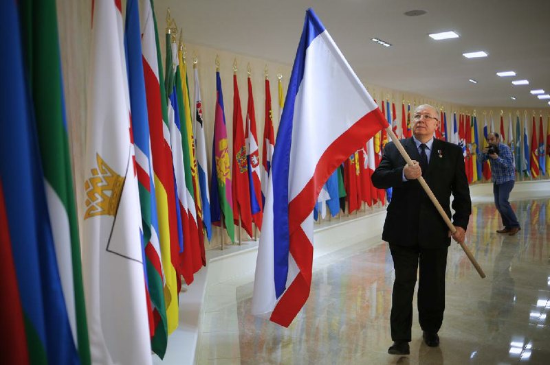 Russian lawmaker, Hero of Russia Alexander Chekalin carries a Crimea flag, to add to a line of Russian regional flags in the hall of the Russian Federation Council building in Moscow, Russia, Monday, March 24, 2014. Two flags, one of Crimea and the other one of Sevastopol have been added to a line of Russian regional flags in the hall of the Federation Council, marking the end of celebrations on the occasion of the region's accession to Russia. (AP Photo/Alexander Zemlianichenko)