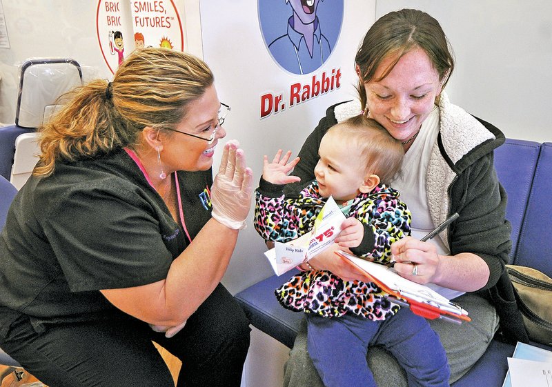 STAFF PHOTO BEN GOFF Stephanie Ableitner, left, a dental hygienist with Pediatric Dental Associates &amp; Orthodontics in Fayetteville, plays Thursday with Aurora Patrick, 1, from Bentonville, while her mother Dominique Patrick fills out consent forms for Aurora to get a free dental screening in the Colgate Bright Smiles, Bright Futures Mobile Dental Van while it makes a visit to the Walmart Supercenter in Bentonville. The mobile unit provides free dental screenings, dental health information and care kits for children up to 12 years old.