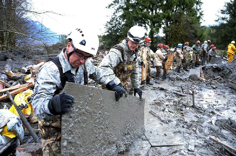 Washington National Guardsmen form a line Friday as they search through mud and debris in Oso, Wash., for signs of missing people a week after a devastating mudslide that has killed at least 25 people and left 90 more unaccounted for. Authorities were delaying an announcement that they said would substantially raise the death toll.