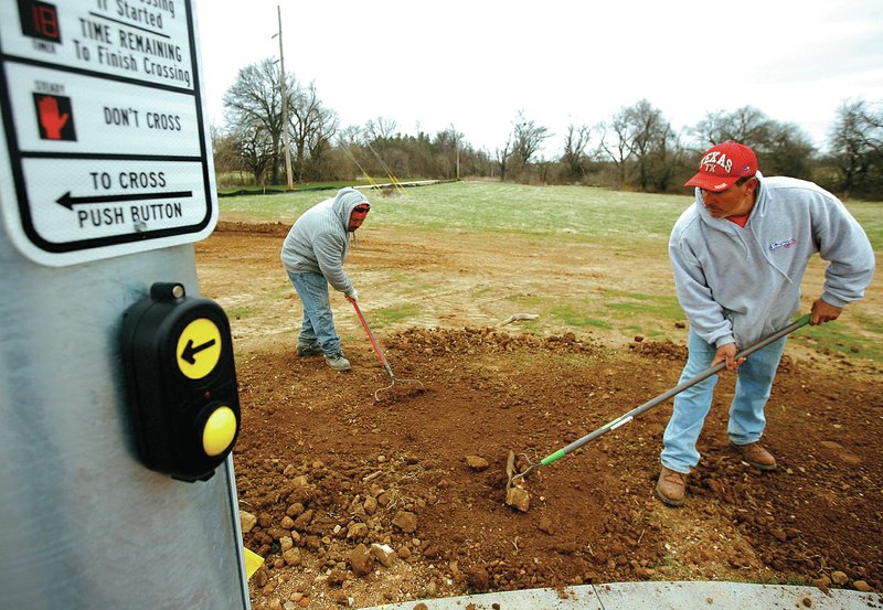 STAFF PHOTO JASON IVESTER Felipe Villagomez, left, and Roberto Estebane, both with Boulder Construction, spread dirt Friday around the edge of the Razorback Greenway near the crossing at Pleasant Grove Road in Rogers.