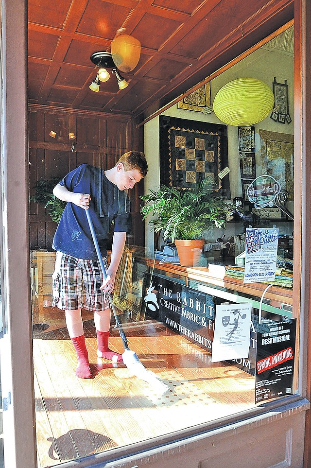 STAFF PHOTO FLIP PUTTHOFF DOWNTOWN WINDOWS Theo Hamrin spruces up a window display Wednesday at The Rabbit's Lair fabric store in downtown Rogers. The effort continues to hire a permanent director for Main Street Rogers.