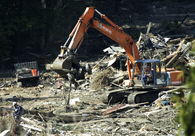 A piece of heavy equipment carries a mangled vehicle Tuesday near Darrington, Wash., at the site of the deadly mudslide that hit the community of Oso, Wash., on March 22. 