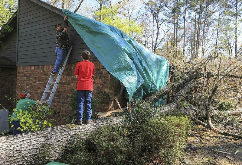 Mike McAllister nails a tarp Friday on his tree-damaged home along Timber Trail in Camden with help from his son Jonathan McCallister, 15, (left) and grandson Peyton Griffen, 11. 