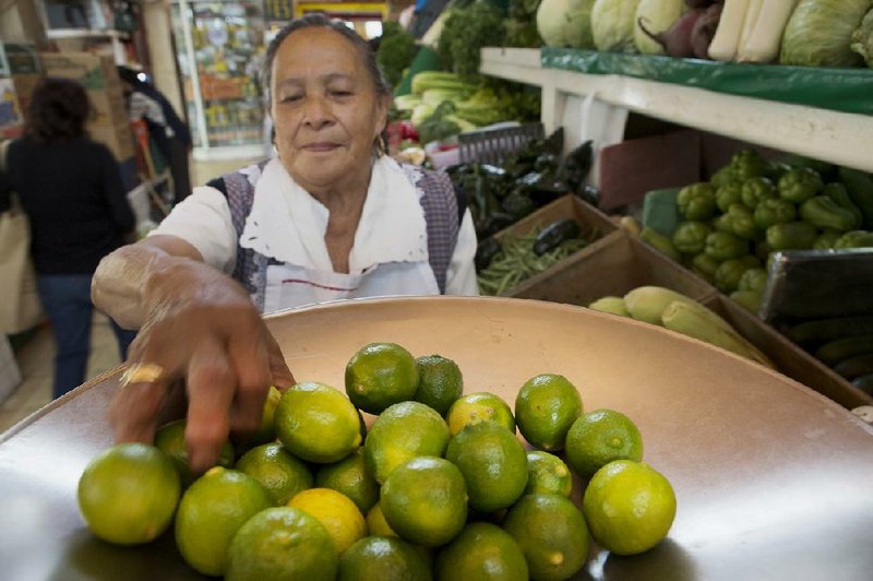 Lilia Olivares, owner of a small stand of fruits and vegetables, weighs limes for sale last week at the Michoacan market in the Condesa neighborhood of Mexico City. Lime growers in the Mexican state of Michoacan have banded together to both set prices of the fruit they sell to packing companies and control supply, spurring inflation. 