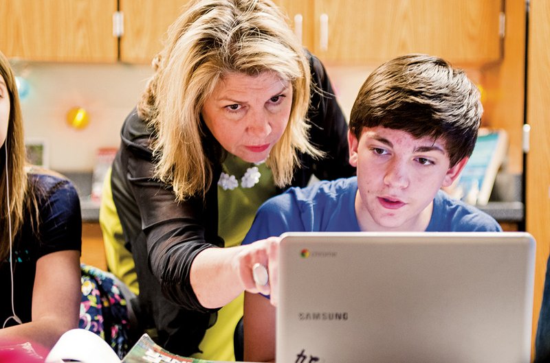 Deana Davis, an English teacher at Cabot Junior High School North, helps eighth-grader Ryan Travis with a project on one of the Chromebooks the district has purchased.