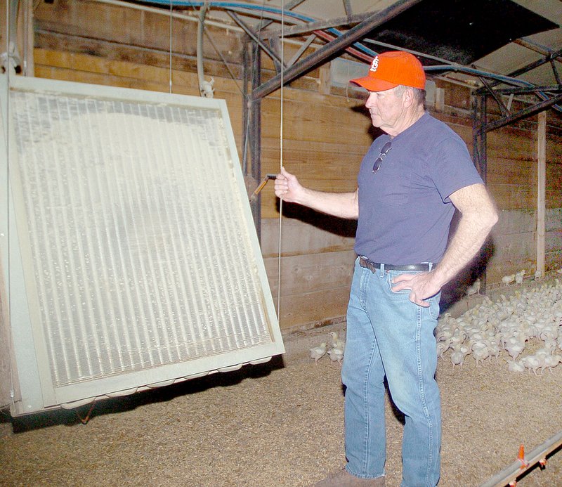 RICK PECK MCDONALD COUNTY PRESS Murphy Biglow stands by a heat exchanger in one of his chicken houses on his farm east of Goodman. Water is heated outside in a furnace and piped to the exchanger where a fan located in back disperses the heat into the air. There are five heat exchangers in each house.